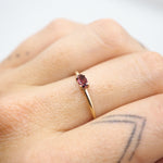 A close-up of a hand wearing a delicate gold ring with a small oval pink gemstone.