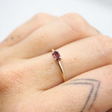 A close-up of a hand wearing a delicate gold ring with a small oval pink gemstone.