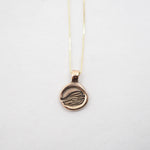 A gold pendant necklace featuring a circular disc pendant with an engraved stylized hand design, suspended from a delicate gold chain against a plain white background.