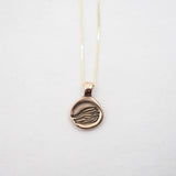 A gold pendant necklace featuring a circular disc pendant with an engraved stylized hand design, suspended from a delicate gold chain against a plain white background.