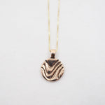 A gold pendant necklace featuring a textured, wavy circular disc pendant, suspended from a delicate gold chain against a plain white background.