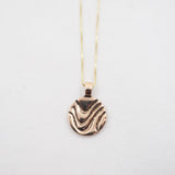 A gold pendant necklace featuring a textured, wavy circular disc pendant, suspended from a delicate gold chain against a plain white background.