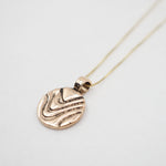 A rose gold pendant necklace featuring a textured, wavy circular disc pendant on a delicate chain, photographed against a clean white background.