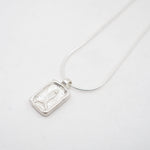 A silver rectangular pendant necklace featuring a textured, carved fish on a delicate silver chain, photographed on a clean white background.