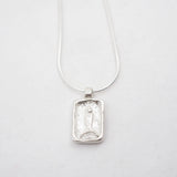 A silver rectangular pendant necklace featuring a textured, carved fish on a delicate silver chain, photographed on a clean white background.