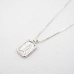 A silver rectangular pendant necklace featuring a textured, carved fish on a delicate silver chain, photographed on a clean white background.