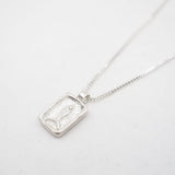 A silver rectangular pendant necklace featuring a textured, carved fish on a delicate silver chain, photographed on a clean white background.
