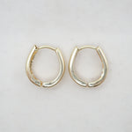 A pair of small gold huggie hoop earrings with a textured, matte finish, displayed on a light off-white background.