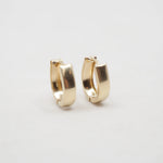 A pair of small gold huggie hoop earrings on a plain light gray background.