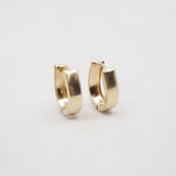 A pair of small gold huggie hoop earrings on a plain light gray background.