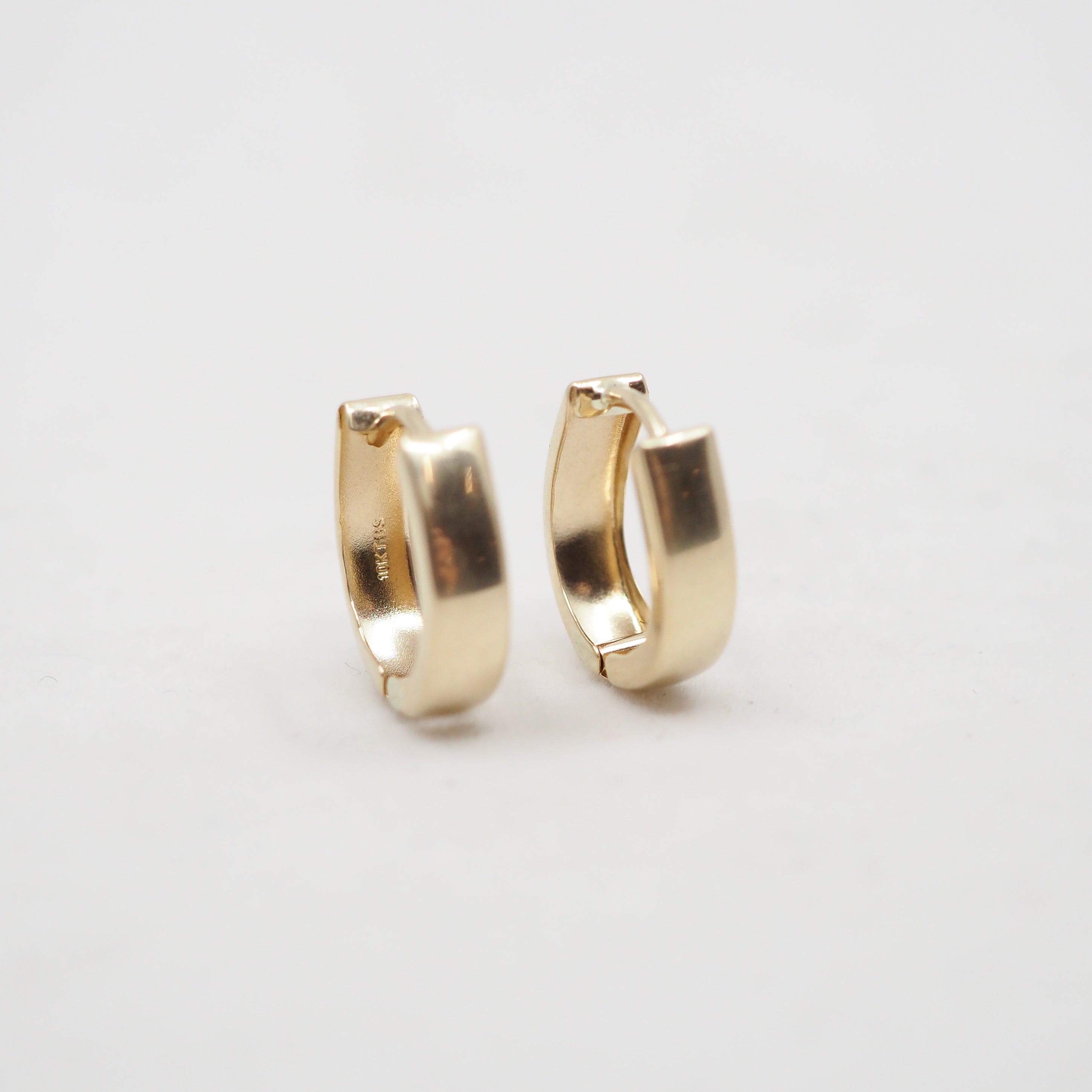 A pair of small gold huggie hoop earrings on a plain light gray background.