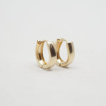 A pair of polished gold huggie hoop earrings on a clean, light gray background.