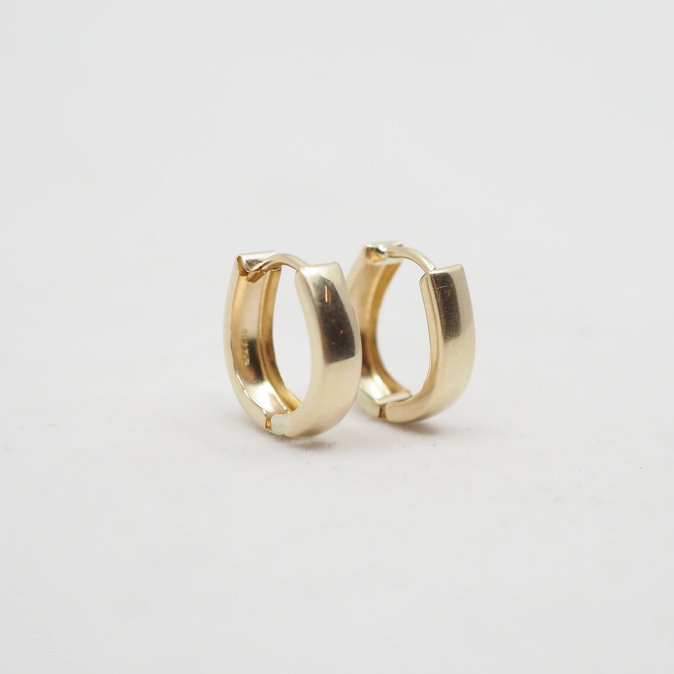 A pair of polished gold huggie hoop earrings on a clean, light gray background.