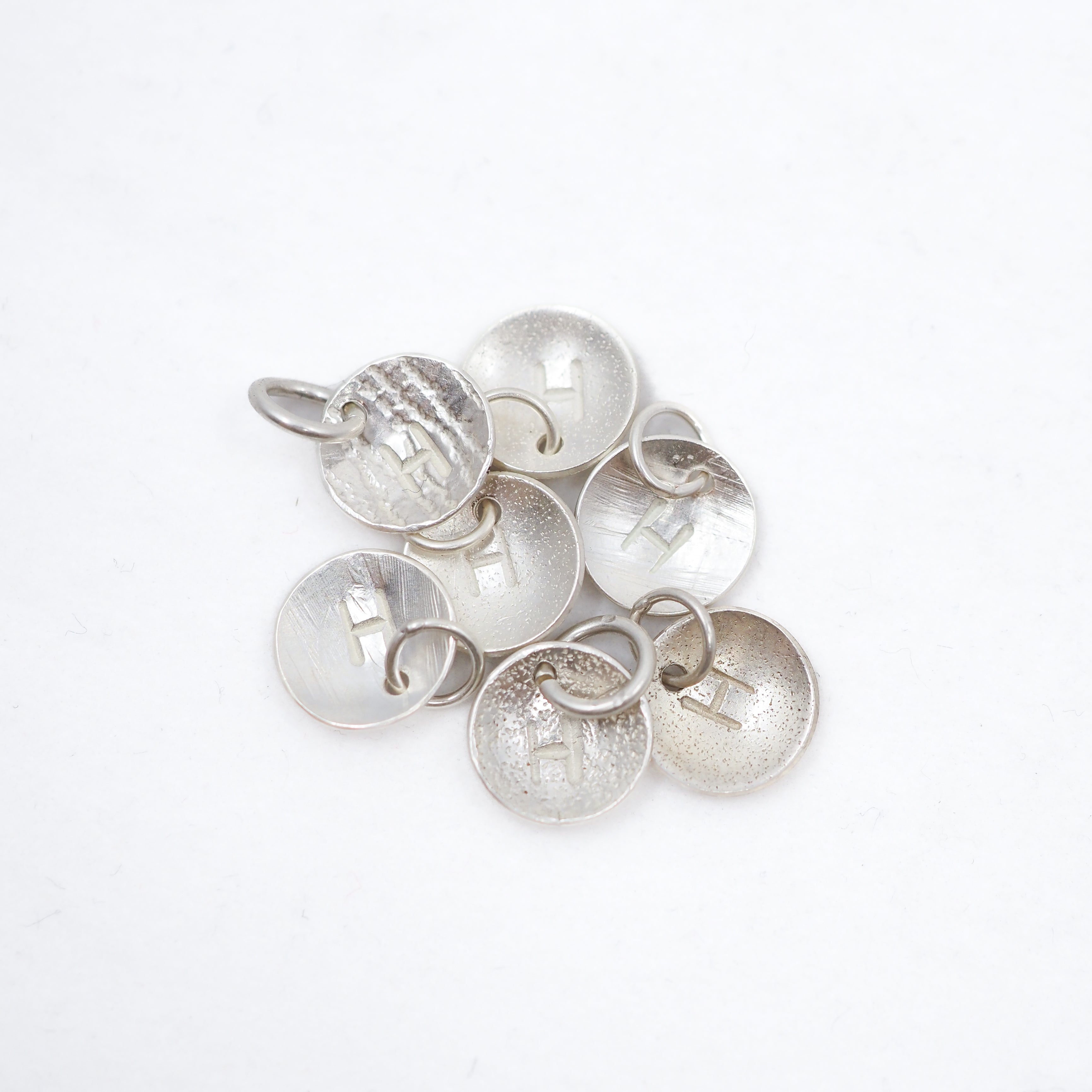 A cluster of textured silver disk charms with small hanging loops, displayed on a clean white background.