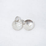 Two small round silver disc charms with textured and brushed finishes, one featuring a raised chevron and the other a heart cutout, shown on a white background.