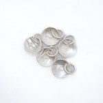Five textured silver disc charms with attached small silver rings, arranged on a plain white background.
