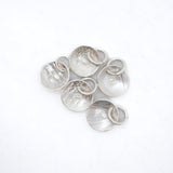 Five textured silver disc charms with attached small silver rings, arranged on a plain white background.