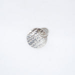 A small hammered silver charm shaped like a round medallion with a small attached loop, photographed on a plain white background.