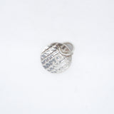 A small hammered silver charm shaped like a round medallion with a small attached loop, photographed on a plain white background.