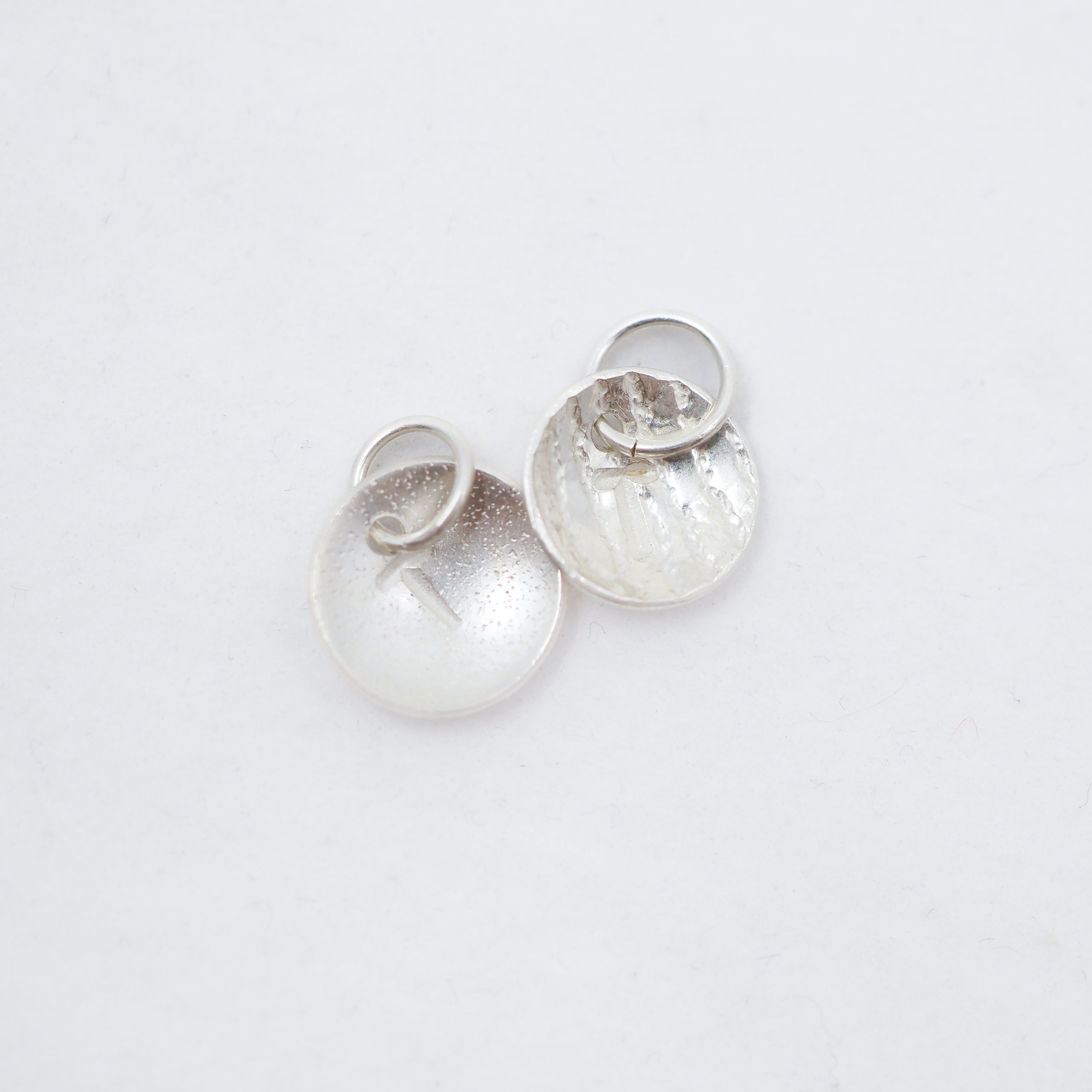 Two small silver discs both with attached jump rings, on a white background.