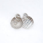 Two silver round disc charms with jump rings, one with a hammered texture and one with a textured matte finish, on a white background.