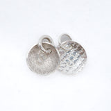 Two silver round disc charms with jump rings, one with a hammered texture and one with a textured matte finish, on a white background.
