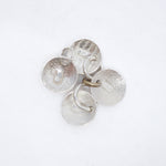 A cluster of five textured silver disc charms with small metal loops, arranged on a plain white background.