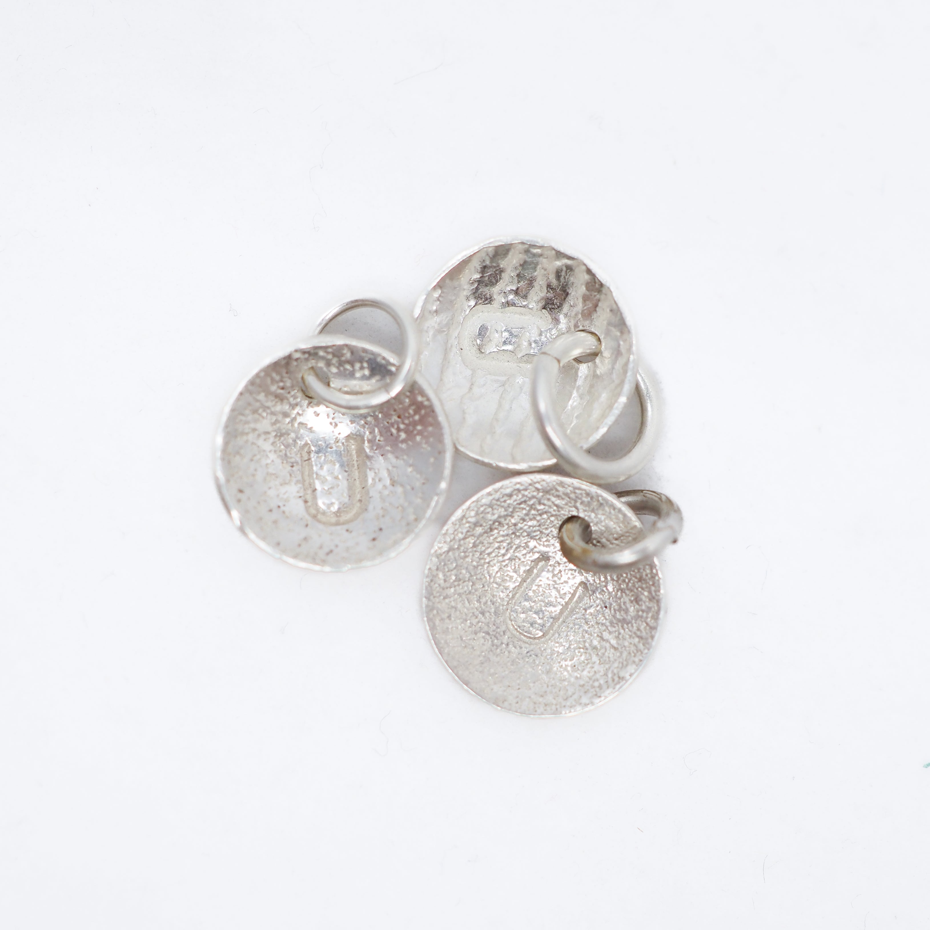 Three textured silver disc charms with attached jump rings, displayed on a clean white background.