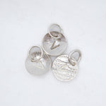 Three textured silver oval charms with jump rings, each featuring a different engraved letter V, arranged on a white background.
