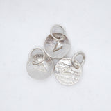 Three textured silver oval charms with jump rings, each featuring a different engraved letter V, arranged on a white background.