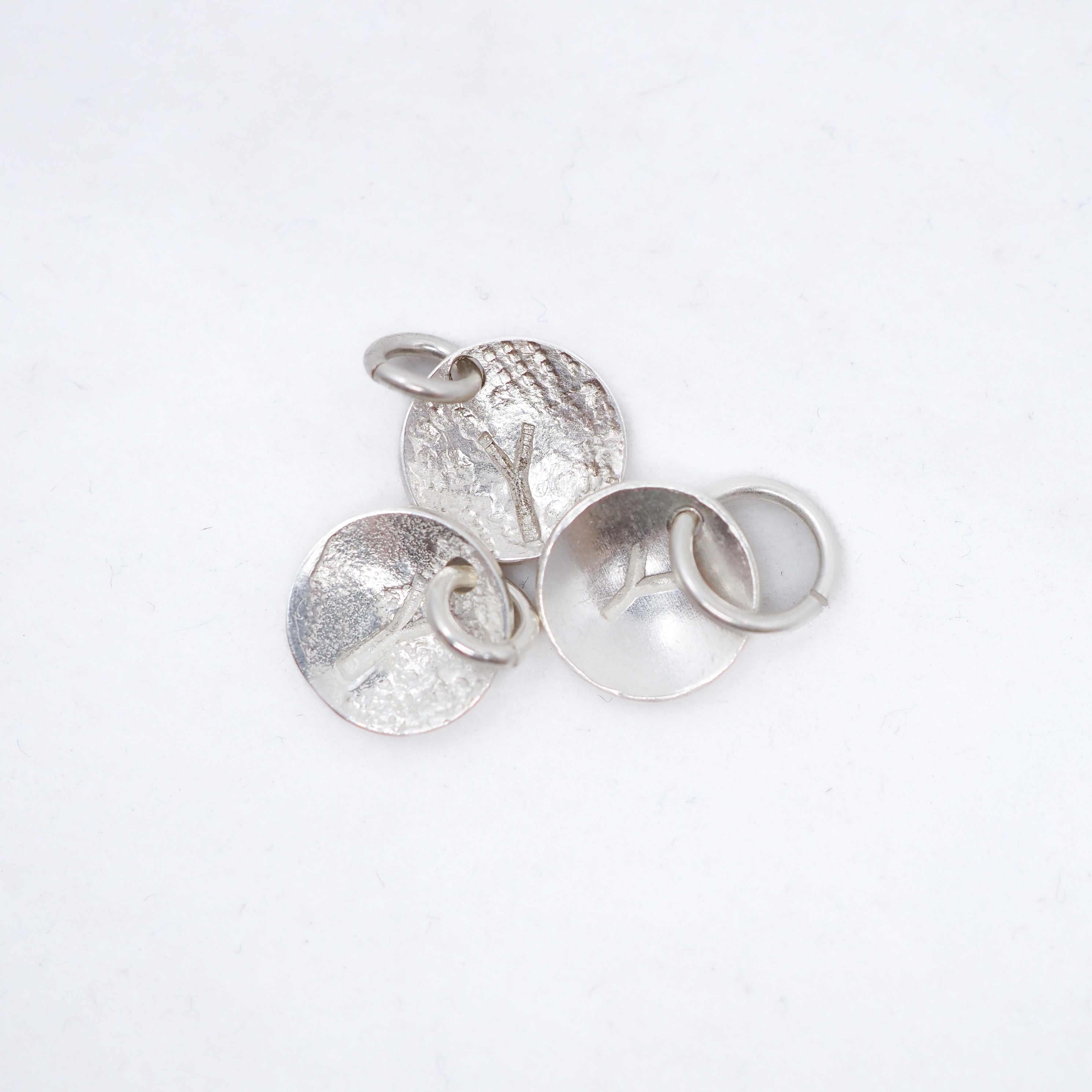 Four textured silver jewelry findings, including two round disc charms with loops and two flat round bases with ring settings, arranged on a clean white background.
