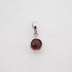 A sterling silver pendant charm featuring a round faceted dark red gemstone in a bezel setting, shown on a plain white background.