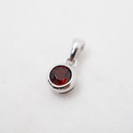 A silver-toned round bezel pendant featuring a faceted dark red gemstone, set against a plain white background.