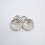 Two textured silver oval charms with a raised letter 'B' and jump rings, displayed on a clean white background.