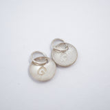 Two small round silver disc charms with attached jump rings, one smooth and one textured, both featuring an engraved letter 'G', on a plain white background.