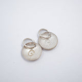 A small silver circular disc charm with a textured, hammered surface and a small attached metal loop, shown on a plain white background.
