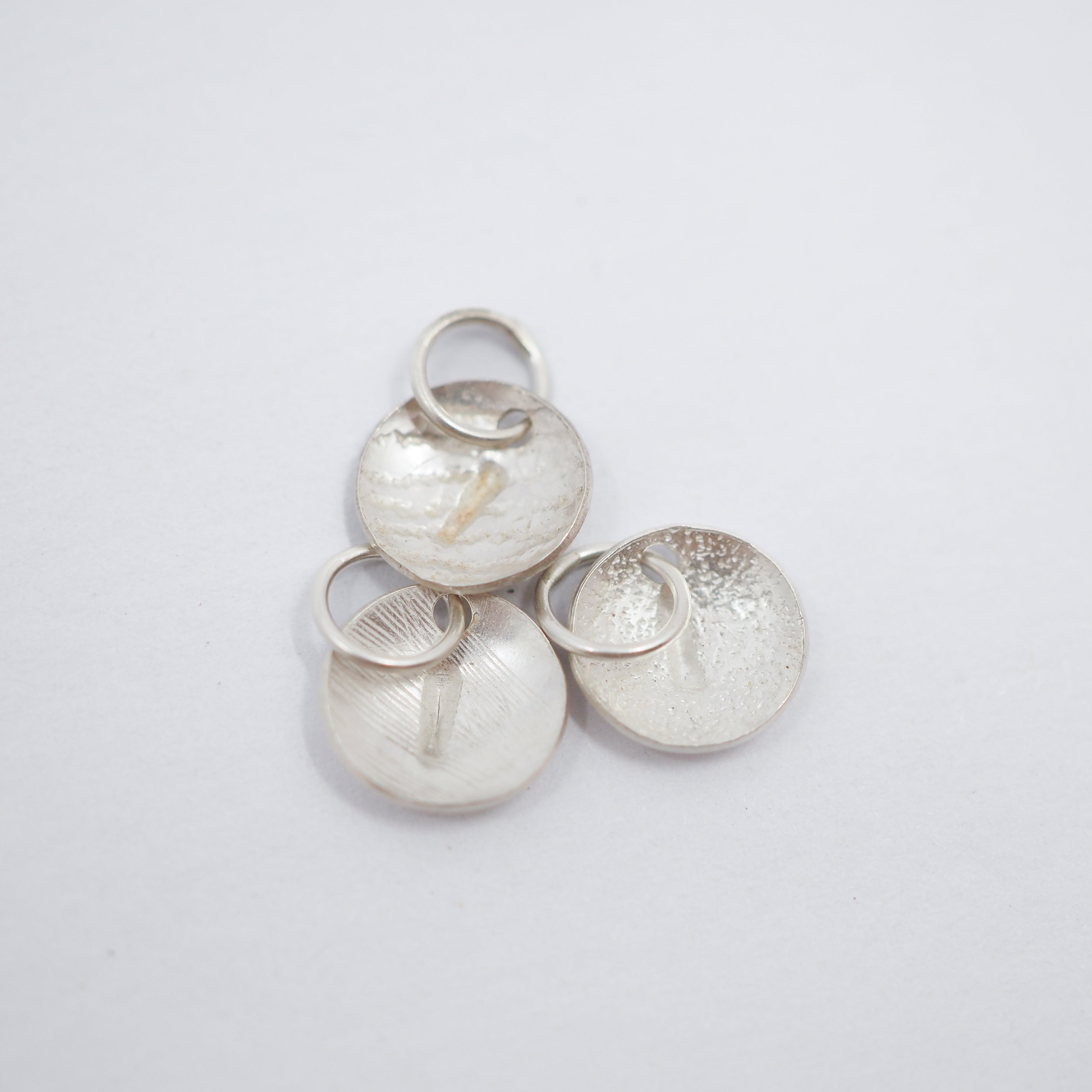 Three textured silver disc charms with attached jump rings, displayed on a clean white background.