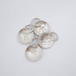 Five silver disk charms with textured finishes and small attached split rings, arranged on a plain light gray background.