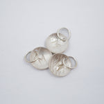 Three textured silver oval charms with lightning bolt details and attached split rings, arranged on a plain light gray background.