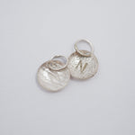 Three textured silver oval charms with lightning bolt details and attached split rings, arranged on a plain light gray background.