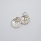 Three textured silver oval charms with lightning bolt details and attached split rings, arranged on a plain light gray background.