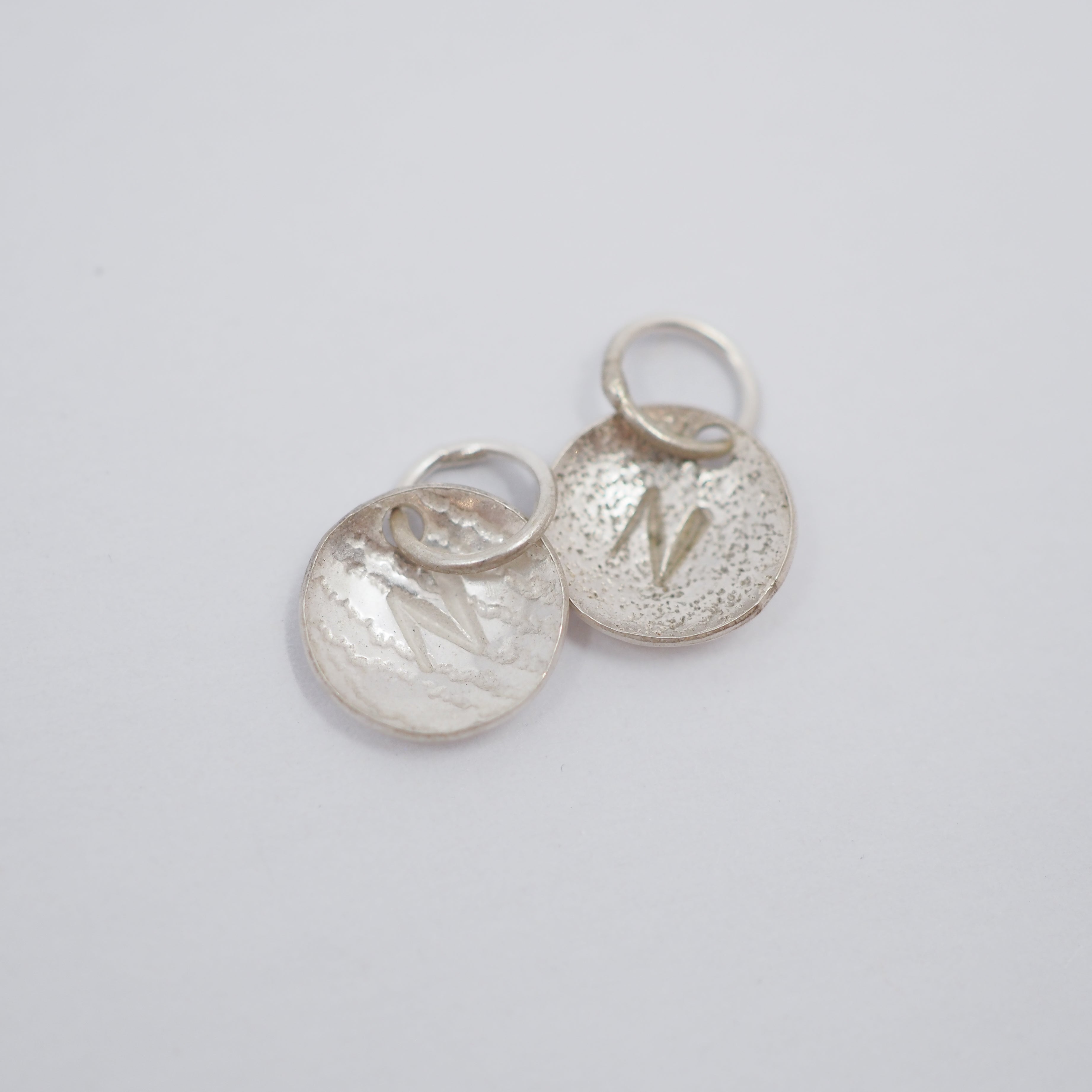 Three textured silver oval charms with lightning bolt details and attached split rings, arranged on a plain light gray background.
