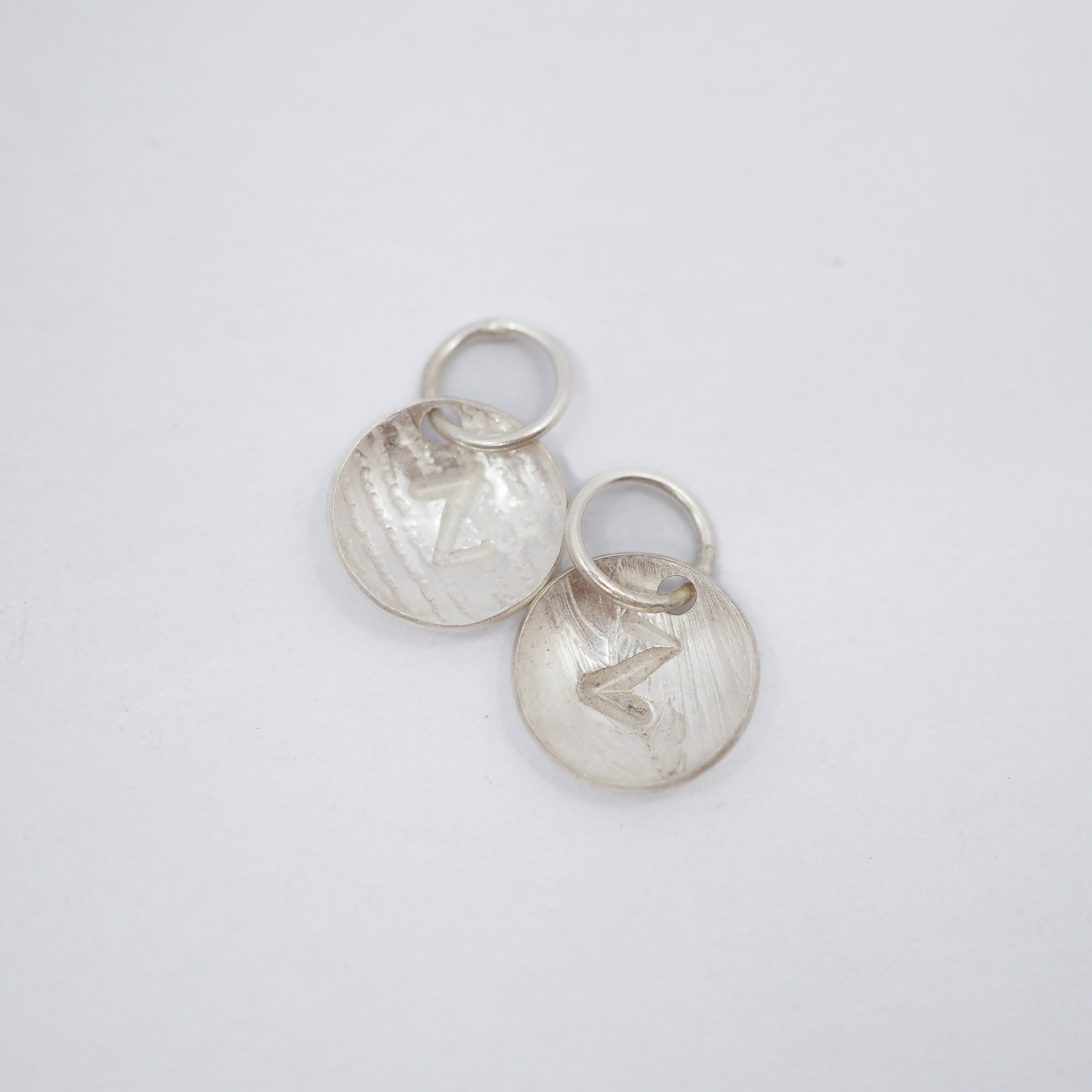 Two textured sterling silver disc charms with engraved letter Z and attached jump rings, displayed on a clean white background.