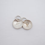 Two small silver oval charms with jump rings, one brushed with a cross and the other textured with a cross, on a light gray background.