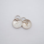 Five textured silver circular jewelry charms with small jump rings, arranged on a plain white background.