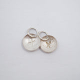 Five textured silver circular jewelry charms with small jump rings, arranged on a plain white background.