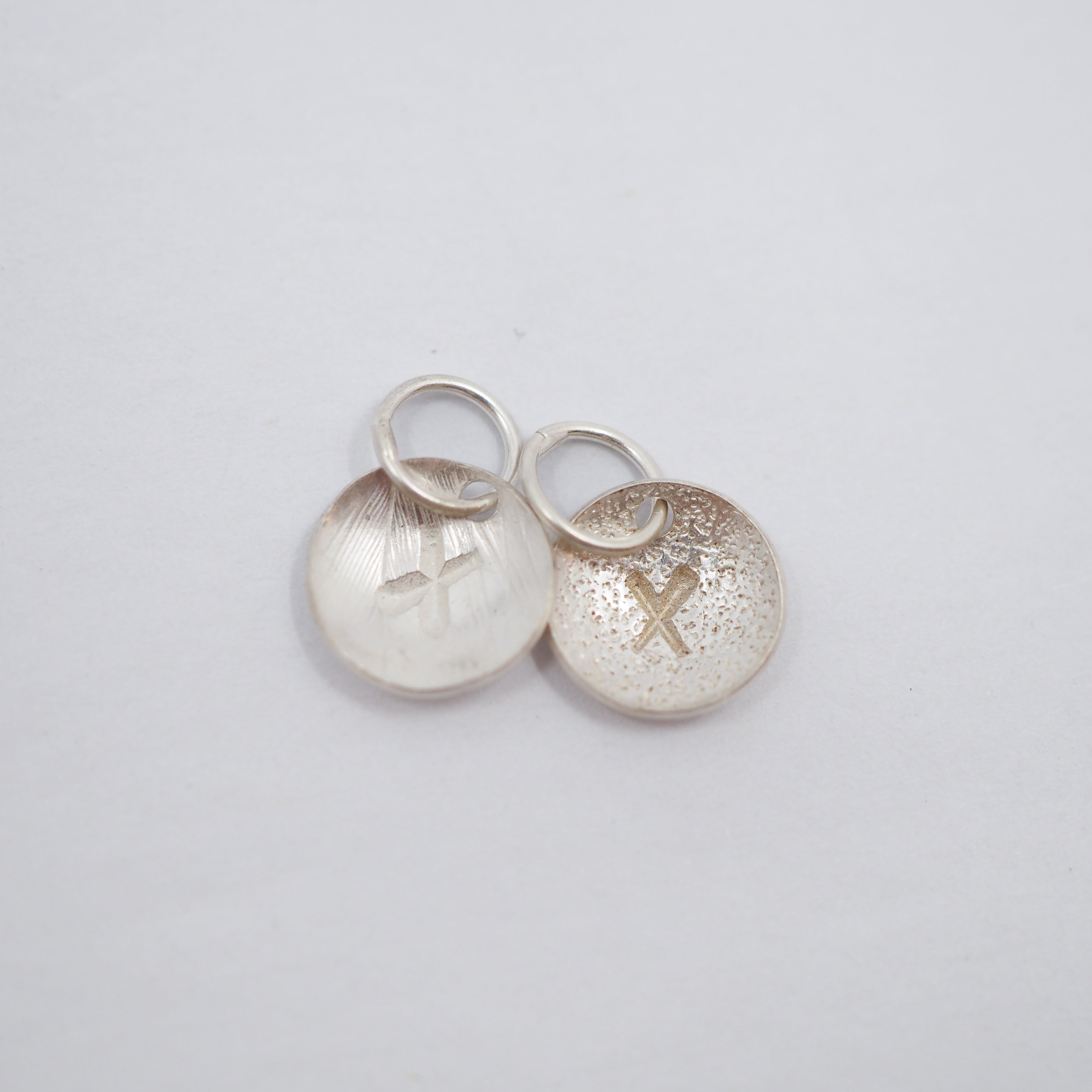 Five textured silver circular jewelry charms with small jump rings, arranged on a plain white background.