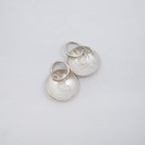 Two textured silver oval charms with a raised letter 'B' and jump rings, displayed on a clean white background.