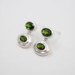 A pair of silver dangle earrings with oval-cut green gemstones, displayed on a clean white background.