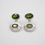A pair of silver drop earrings with oval green gemstones, displayed on a clean white background.